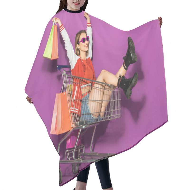 Personality  Beautiful Happy Young Woman In Sunglasses Holding Paper Bags And Sitting In Shopping Trolley On Violet  Hair Cutting Cape