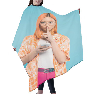 Personality  Secrecy, Silent Please, Young Asian Woman Holding Smartphone, Looking At Camera And Showing Hush Sign On Blue Background, Dyed Red Hair, Trendy Eyeglasses, Orange Shirt, Summer Fashion Hair Cutting Cape