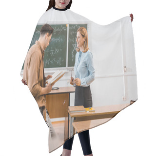 Personality  Male Student Holding Book Near Smiling Female Teacher In Classroom Hair Cutting Cape