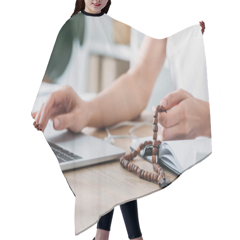 Personality  cropped view of businesswoman using laptop and holding rosary beads at workplace hair cutting cape