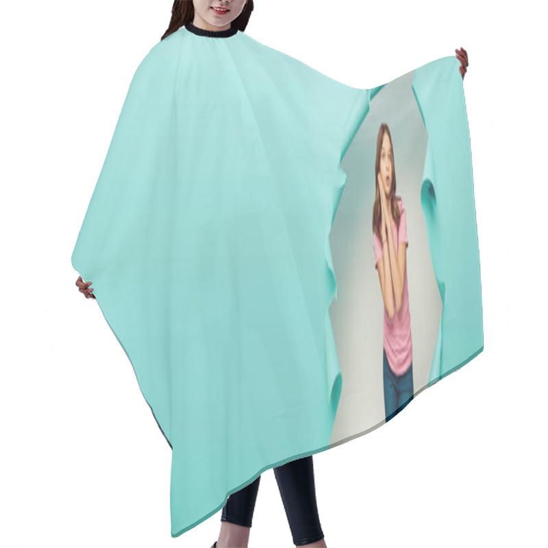 Personality  Shocked preteen girl in casual clothes looking at camera during child protection day celebration behind hole in blue paper background, banner  hair cutting cape