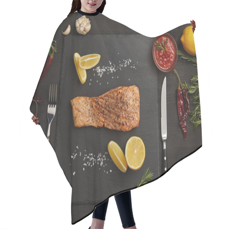 Personality  top view of grilled salmon steak with pieces of lemon, arranged ingredients around and cutlery on black surface hair cutting cape