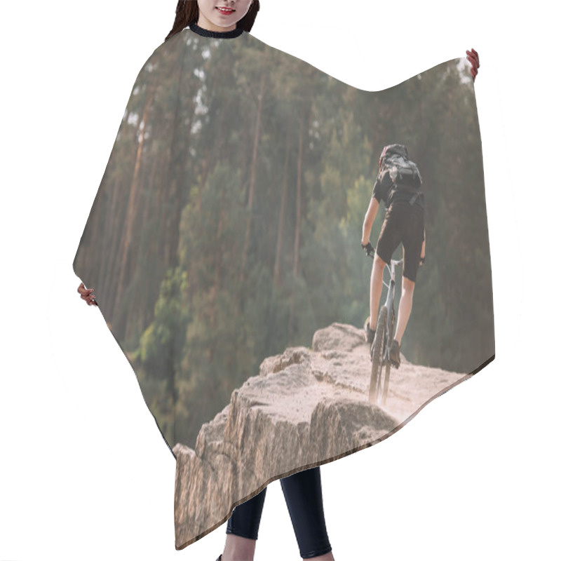 Personality  back view of young trial biker riding on rocks outdoors hair cutting cape