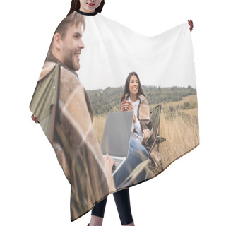 Personality  Cheerful African American Woman In Blanket Holding Cup Near Boyfriend With Laptop On Blurred Foreground During Camping  Hair Cutting Cape