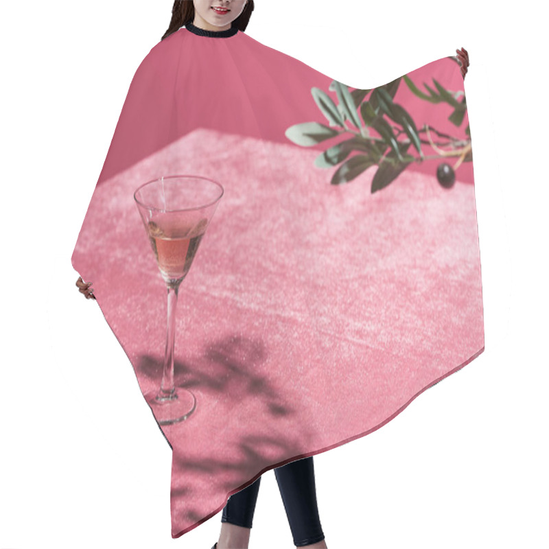 Personality  selective focus of olive tree branch near rose wine in glass on velour pink cloth isolated on pink, girlish concept hair cutting cape