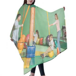 Personality  Smiling Parents Looking At Happy Kids Swinging On Swings In Indoor Play Center Hair Cutting Cape