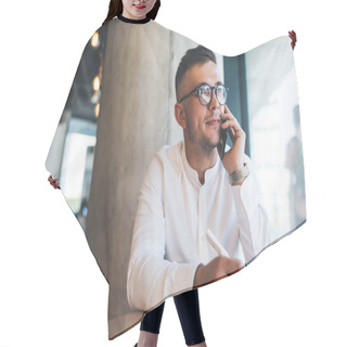Personality  Focused Young Male Freelancer Wearing White Shirt And Eyeglasses Writing Notes During Phone Call While Working Remotely In Creative Cafeteria Hair Cutting Cape