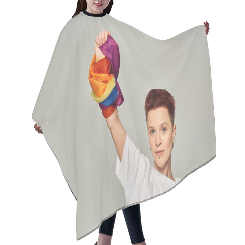 Personality  confident redhead bigender person in white t-shirt and jeans standing with LGBT flag on grey hair cutting cape