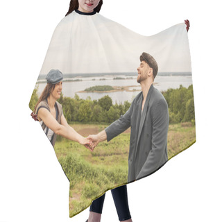 Personality  Positive And Fashionable Brunette Woman In Newsboy Cap And Vest Holding Hand Of Bearded Boyfriend In Jacket While Standing With Scenic Landscape At Background, Fashionable Couple In Countryside Hair Cutting Cape