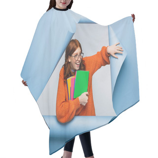 Personality  Amazed Redhead Student In Orange Sweater And Glasses Holding Notebooks On Blue Ripped Paper Background  Hair Cutting Cape