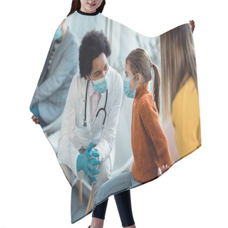 Personality  Black Female Doctor Talking To A Small Girl Who Is Sitting With Her Mother At Hospital Waiting Room And Wearing Protective Face Mask Due To Coronavirus Pandemic. Hair Cutting Cape