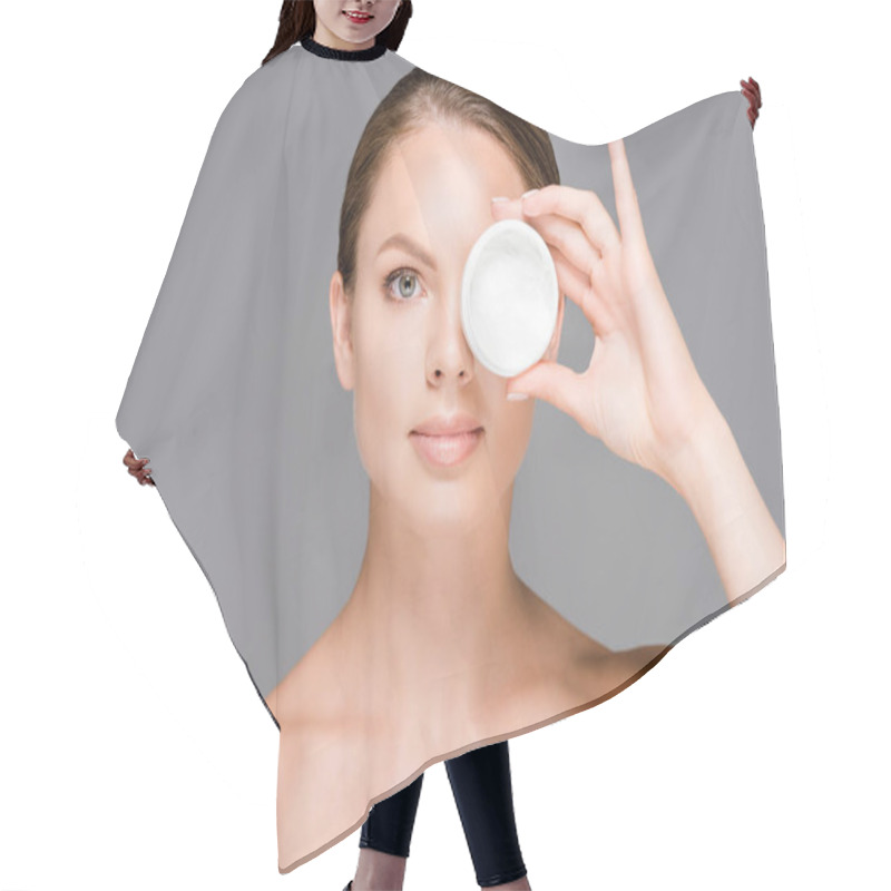 Personality  portrait of beautiful young woman covering eye with face cream in jar isolated on grey hair cutting cape