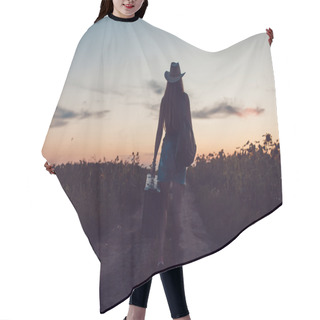 Personality  Girl In A Cowboy Hat Standing With A Suitcase On The Road In The Sunflower Field. Waiting For Help. Sunset. Hair Cutting Cape