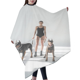 Personality  Stylish Woman In Bodysuit And Leather Boots With Dobermans On Chain Leashes On Grey Background With Shadows Hair Cutting Cape