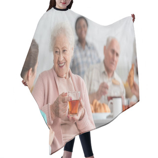 Personality  Positive Senior Woman Holding Tea While Talking To Blurred Nurse In Nursing Home  Hair Cutting Cape