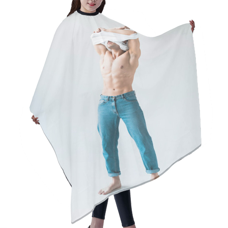 Personality  muscular man covering face while taking off white t-shirt and standing on white  hair cutting cape