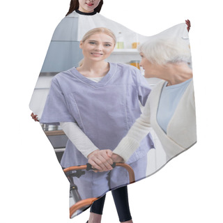 Personality  Smiling Nurse Looking At Camera Near Aged Woman With Medical Walkers Hair Cutting Cape