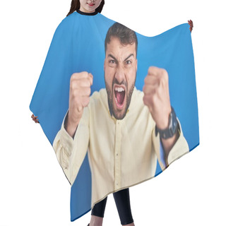 Personality  Handsome Hispanic Man Standing Over Blue Background Angry And Mad Raising Fists Frustrated And Furious While Shouting With Anger. Rage And Aggressive Concept.  Hair Cutting Cape