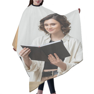 Personality  Cheerful Concierge In Trendy Casual Clothes And With Wavy Brunette Hair Looking At Notebook Near Computer Monitor While Working At Reception Desk In Contemporary Hotel, Digital Nomad  Hair Cutting Cape