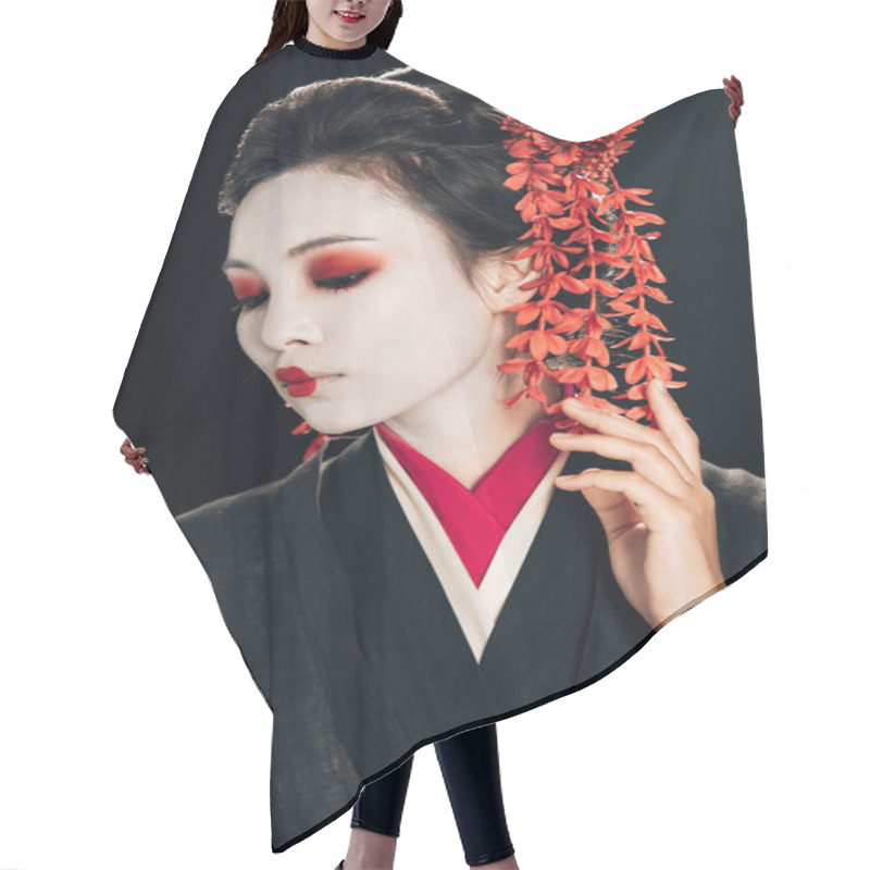 Personality  portrait of beautiful geisha in black and red kimono and flowers in hair looking down isolated on black hair cutting cape