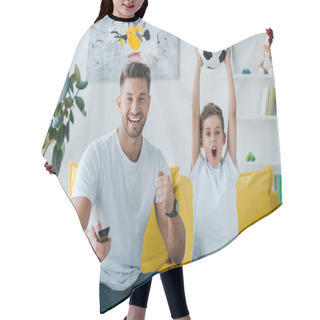 Personality  Cheerful Father Holding Remote Controller Near Son With Football Above Head  Hair Cutting Cape