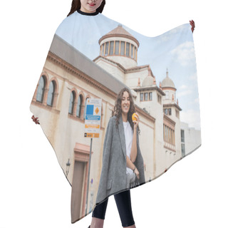 Personality  Positive Young Woman In Casual Grey Jacket Holding Fresh Orange And Leash While Looking At Camera With Historical Landmark At Background On City Street In Barcelona, Spain, Ancient Building  Hair Cutting Cape