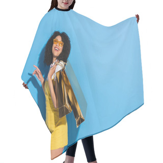 Personality  Excited African American Woman In Yellow Eyeglasses Posing With Shiny Shopping Bags On Blue Hair Cutting Cape