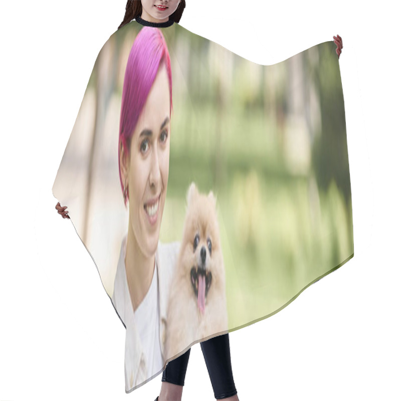 Personality  smiley and trendy woman with cute pomeranian spitz in hands looking at camera in park, banner hair cutting cape