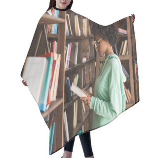 Personality  Side View Of African American Student In Eyeglasses Reading Book Near Blurred Bookcase On Foreground Hair Cutting Cape