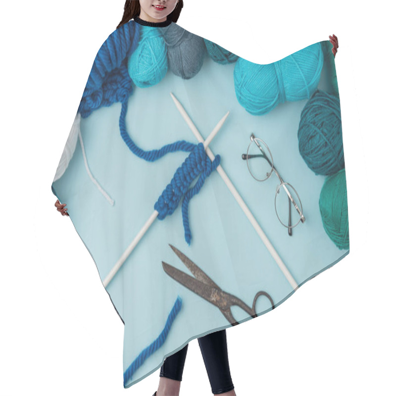 Personality  close up view of yarn, knitting needles, eyeglasses and scissors on blue backdrop hair cutting cape