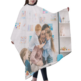 Personality  Interracial Kids Hugging Happy Teacher At Table In Classroom Hair Cutting Cape