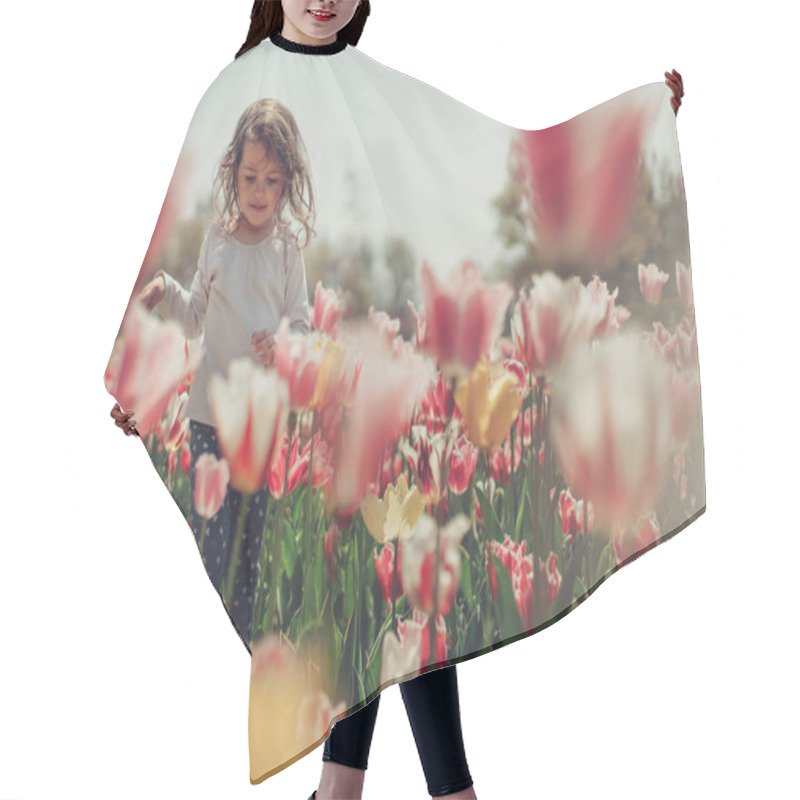 Personality  Little beautiful girl in flowers park and blooming tulips hair cutting cape