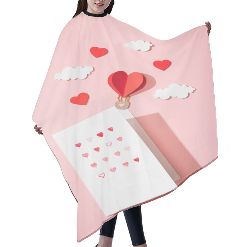 Personality  top view of greeting card with hearts in white envelope near paper heart shaped air balloon in clouds on pink hair cutting cape