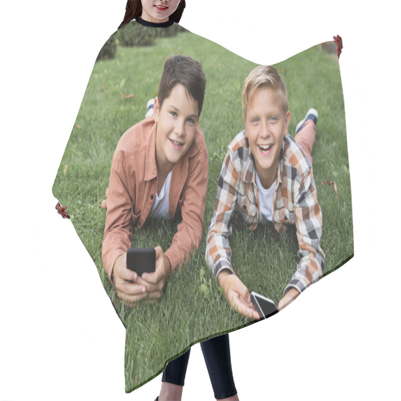 Personality  Two Cheerful Brothers Lying On Grass, Holding Smartphones And Looking At Camera Hair Cutting Cape