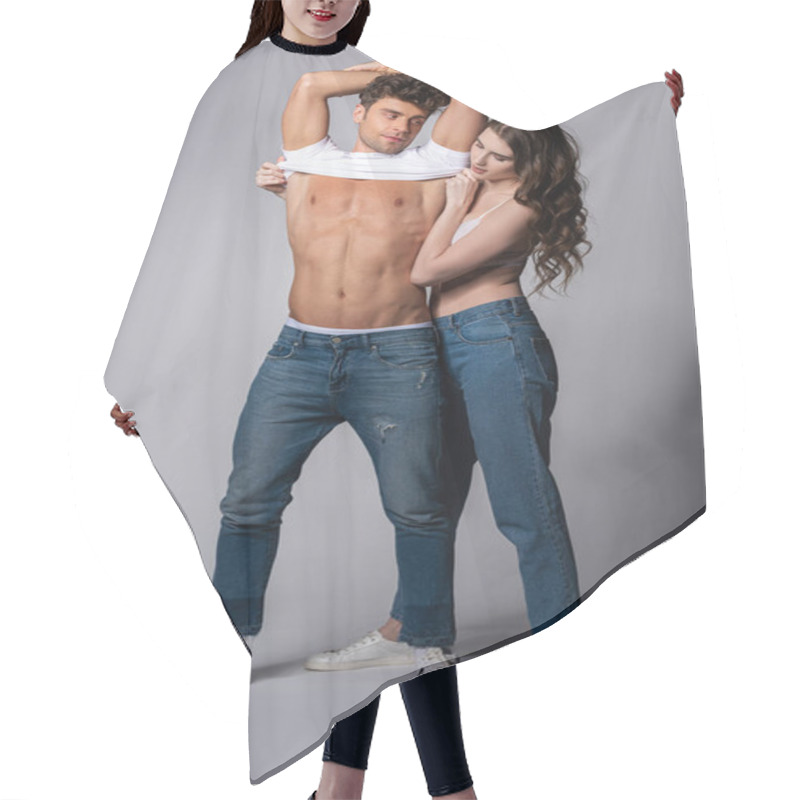 Personality  attractive girl in bra taking off white t-shirt of muscular boyfriend on grey  hair cutting cape