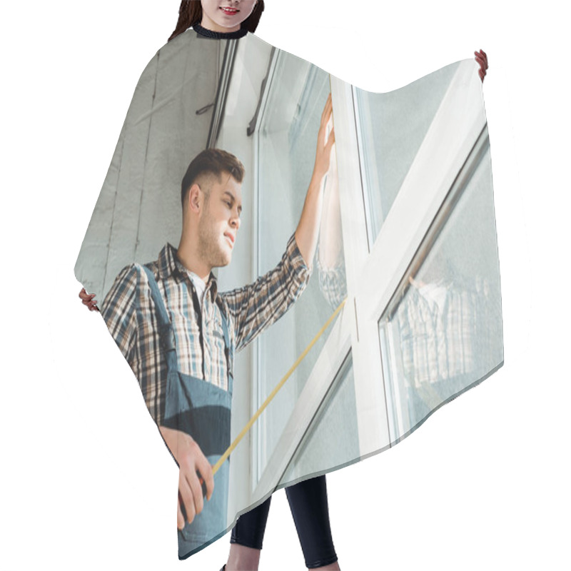 Personality  low angle view of installer standing near windows and holding measuring tape hair cutting cape