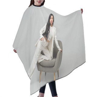 Personality  Full Length Of Young Asian Woman Leaning On Armchair While Posing With Hand In Pocket On Grey Hair Cutting Cape