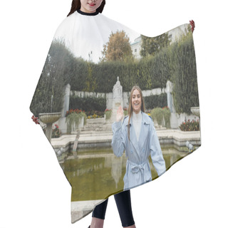 Personality  Smiling Young Woman In Blue Trench Coat Waving Hand Near Fountain In Green Park  Hair Cutting Cape