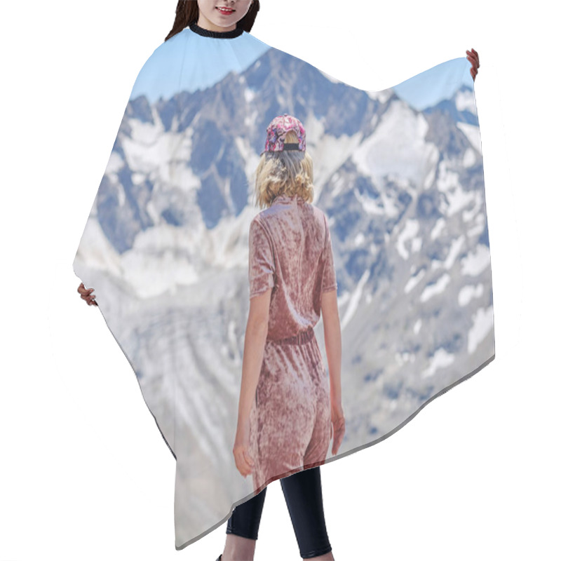 Personality  Rear View Of A Blonde In A Baseball Cap Posing Against A Background Of Snowy Mountain Peaks Of The Caucasus. Hair Cutting Cape