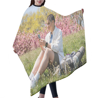 Personality  Smiling Young Short Haired Female Traveler Using Smartphone While Sitting Near Backpack With Travel Equipment On Grassy Hill With Nature At Background, Curious Hiker Exploring New Landscapes Hair Cutting Cape