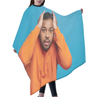 Personality  Worried African American Young Man In Orange Outfit Holding To Head With Hands On Blue Background Hair Cutting Cape