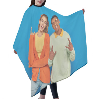 Personality  Excited And Young Interracial Couple In Casual Attire Gesturing On Blue Backdrop, Showing Rock Sign Hair Cutting Cape