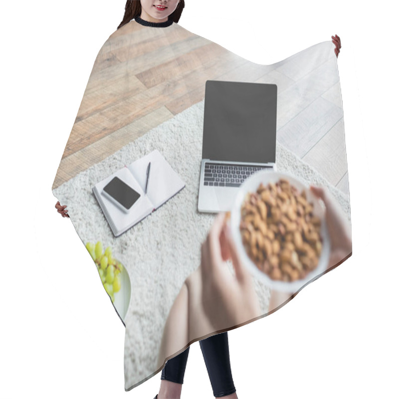 Personality  partial view of blurred freelancer holding bowl with almonds near gadgets and fresh grape on floor hair cutting cape