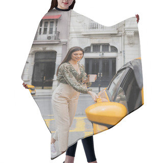 Personality  Smiling Young Woman With Long Hair Holding Coffee In Paper Cup While Standing In Trendy Outfit With Handbag On Chain Strap And Opening Door Of Yellow Cab On Blurred Urban Street In Istanbul  Hair Cutting Cape