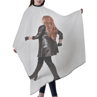 Personality  Full Length Portrait Of Girl With Long Red Hair Wearing Dark Leather Coat, Corset And Boots. Standing Pose Facing Back View With  Magical Hand Gestures Against A  Studio Background. Hair Cutting Cape