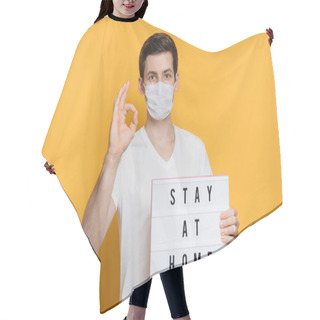 Personality  Young Man In Protective Mask Doing Ok Sign And Showing Board With Stay Home Text To Prevent Coronavirus Infection. Isolated On Yellow Background. COVID-19  Quarantine And Self Isolation Concept. Hair Cutting Cape