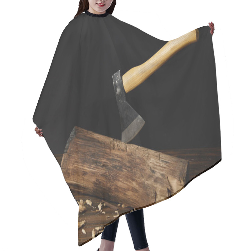 Personality  log with sticking axe and wooden pieces at table on black background hair cutting cape
