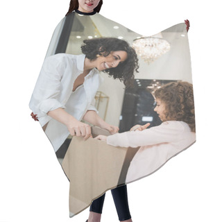 Personality  Excited Middle Eastern Woman With Brunette Hair In White Shirt And Happy Little Girl Looking Inside Of Shopping Bag In Bridal Salon, Mother And Daughter, Bridal Shopping, Happiness  Hair Cutting Cape