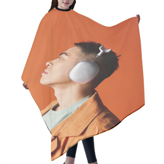 Personality  A Handsome Asian Man In Stylish Attire Listening To Music With Headphones On His Ears Against An Orange Studio Background. Hair Cutting Cape