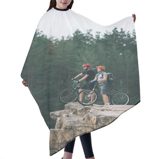 Personality  Side View Of Happy Young Trial Bikers Standing On Rocky Cliff With Blurred Pine Forest On Background And Looking Away Hair Cutting Cape
